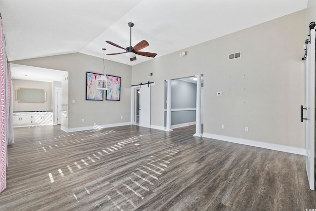 unfurnished living room with ceiling fan, a barn door, dark wood-type flooring, and lofted ceiling