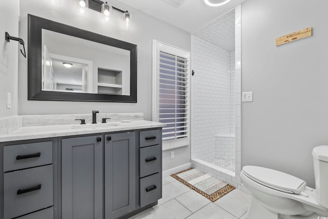 bathroom with toilet, a tile shower, tile patterned floors, and vanity