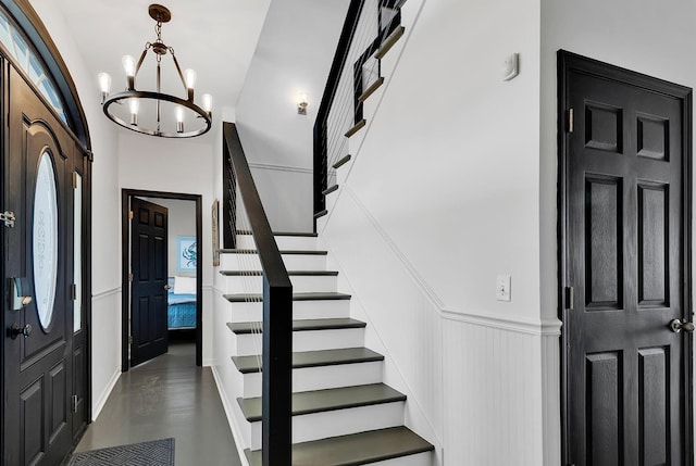 entryway featuring a wainscoted wall, a notable chandelier, a decorative wall, and stairs