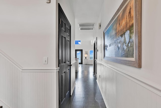 hallway with a wainscoted wall, dark wood-style floors, and visible vents