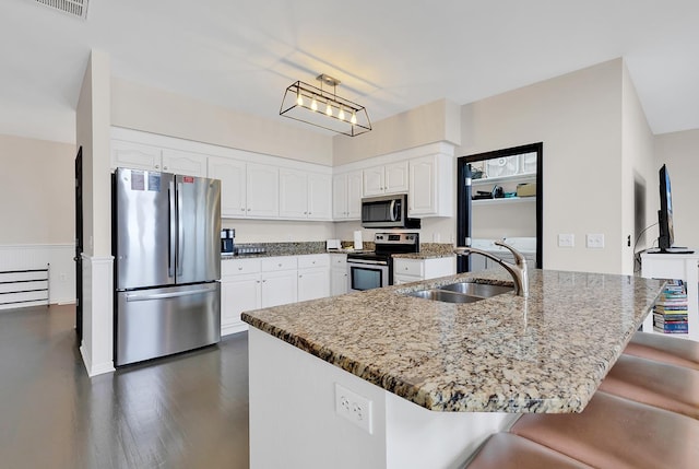 kitchen with stone countertops, a breakfast bar, a sink, white cabinetry, and appliances with stainless steel finishes