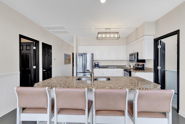 kitchen featuring white cabinets, a kitchen bar, appliances with stainless steel finishes, light stone countertops, and sink