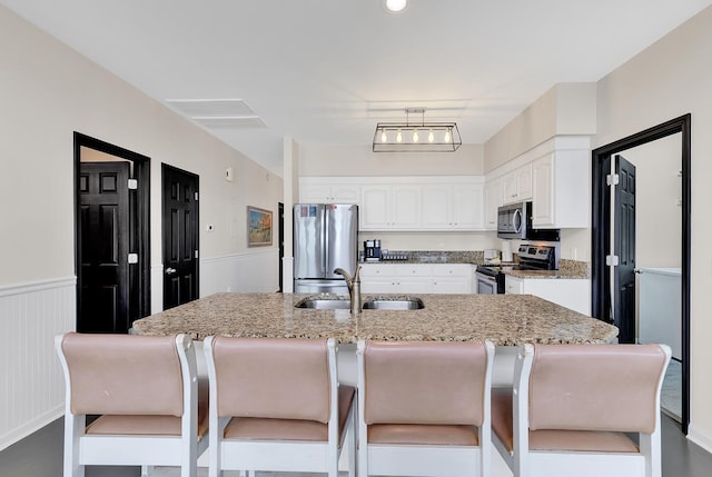 kitchen featuring a breakfast bar area, a sink, white cabinetry, appliances with stainless steel finishes, and wainscoting