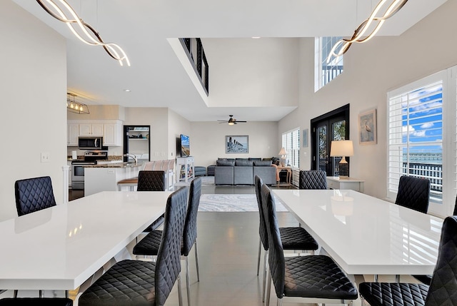 dining space featuring sink, ceiling fan, and a towering ceiling