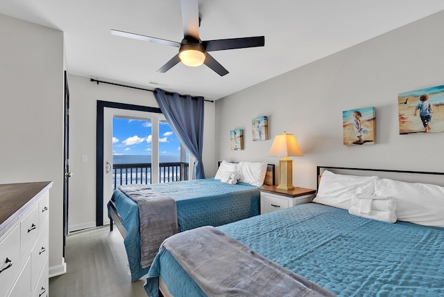 bedroom featuring access to exterior, a water view, visible vents, ceiling fan, and wood finished floors