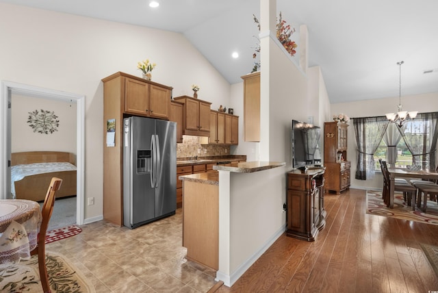 kitchen with a notable chandelier, stainless steel fridge with ice dispenser, kitchen peninsula, high vaulted ceiling, and light wood-type flooring