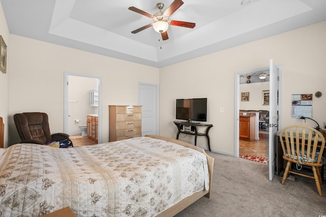 carpeted bedroom with ensuite bath, a raised ceiling, and ceiling fan