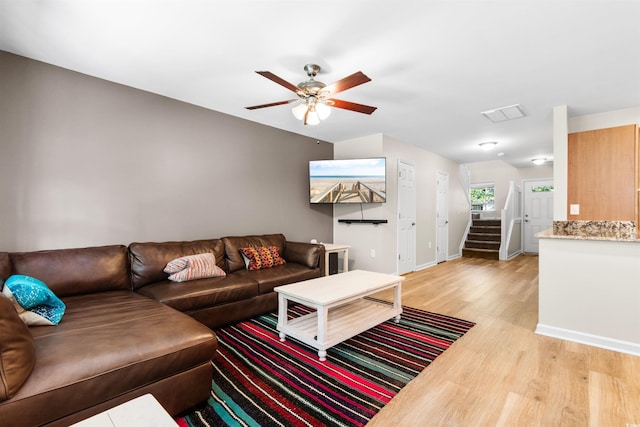 living room with visible vents, light wood-style flooring, ceiling fan, baseboards, and stairs