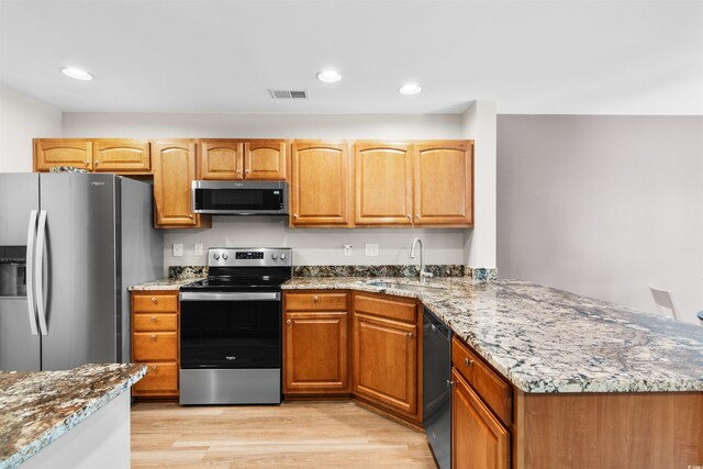 kitchen with appliances with stainless steel finishes, light stone counters, sink, and light wood-type flooring