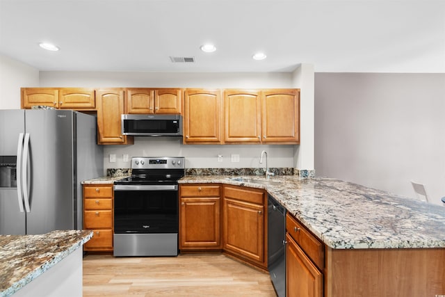 kitchen with visible vents, appliances with stainless steel finishes, light stone counters, light wood-type flooring, and a sink