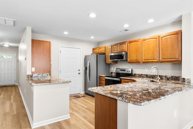 kitchen featuring stone counters, light wood-style flooring, stainless steel appliances, a peninsula, and a sink