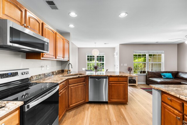 kitchen with sink, stainless steel appliances, light wood-type flooring, and light stone counters