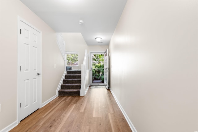 corridor with baseboards, stairway, and light wood finished floors