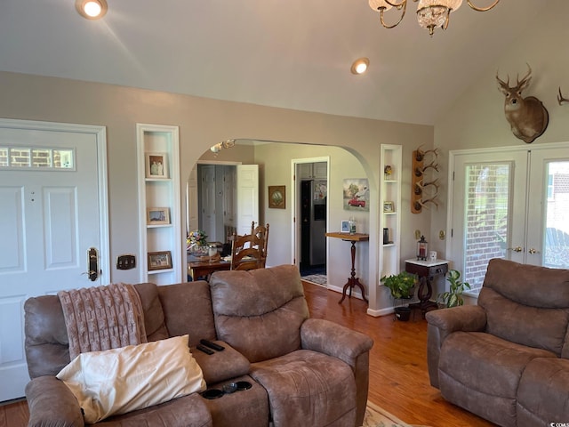 living room featuring light wood-type flooring, a chandelier, lofted ceiling, french doors, and built in features