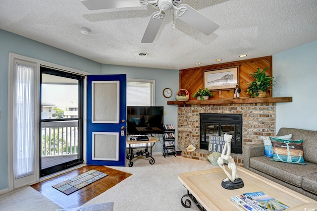 living room featuring a textured ceiling, wood walls, carpet floors, a fireplace, and ceiling fan