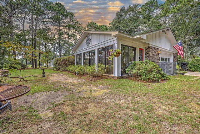 property exterior at dusk featuring a lawn and a sunroom