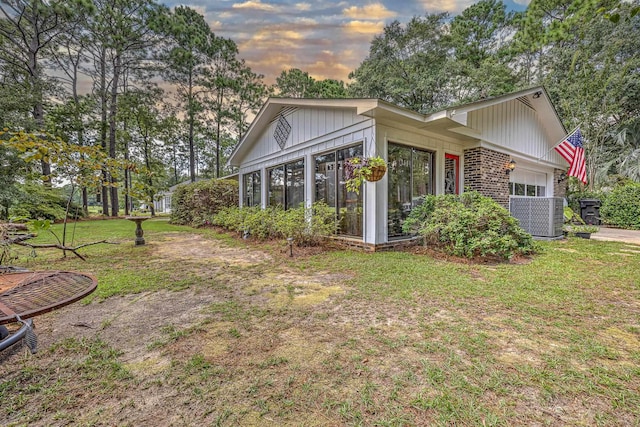 view of property exterior featuring a garage, brick siding, a sunroom, and a yard