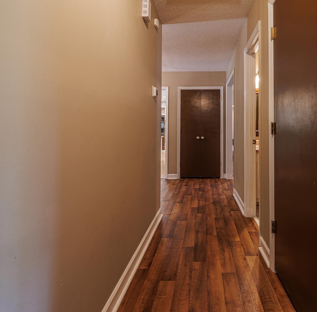 hall featuring dark wood-style floors, a textured ceiling, and baseboards