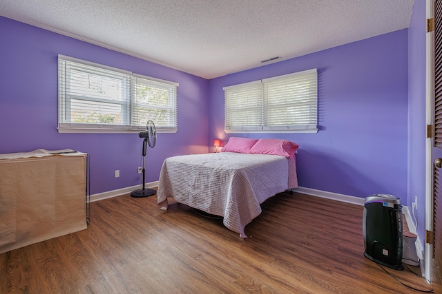 bedroom with visible vents, dark wood finished floors, a textured ceiling, and baseboards