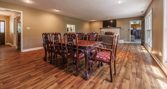 dining space with a brick fireplace, a healthy amount of sunlight, and wood-type flooring