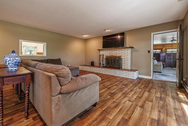 living room with wood-type flooring, a textured ceiling, and a brick fireplace