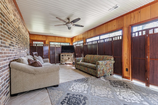 tiled living room featuring wood walls, brick wall, and ceiling fan