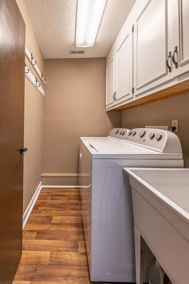 laundry area featuring a textured ceiling, washer and clothes dryer, cabinets, and light wood-type flooring