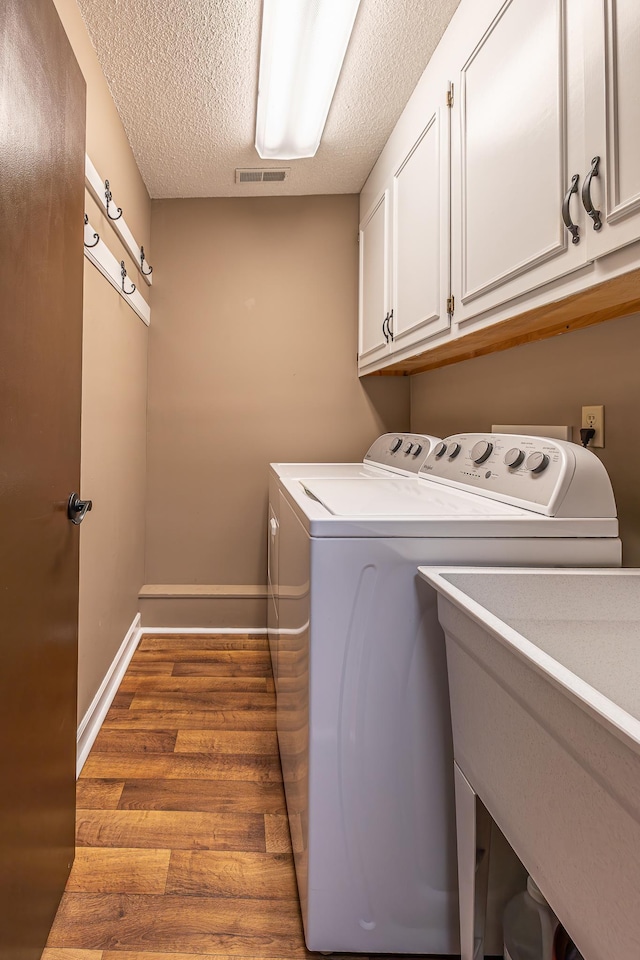 clothes washing area featuring cabinet space, baseboards, a textured ceiling, light wood-style floors, and separate washer and dryer