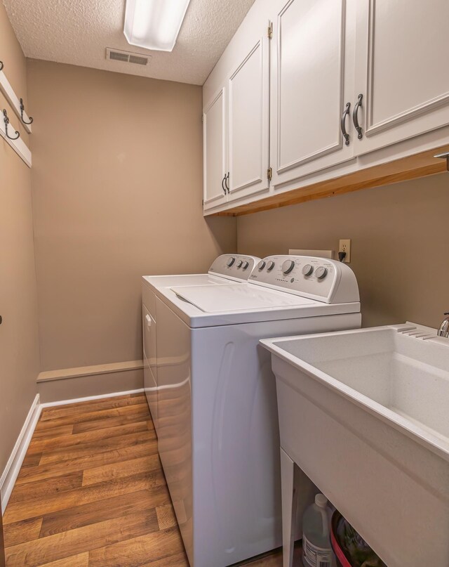 clothes washing area with sink, cabinets, light hardwood / wood-style floors, a textured ceiling, and washer and dryer