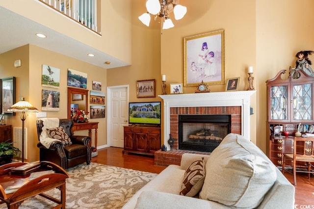 living room with a towering ceiling, hardwood / wood-style floors, ceiling fan, and a brick fireplace