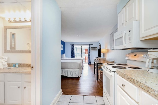 kitchen featuring white cabinetry, a wall mounted air conditioner, white appliances, and light tile patterned flooring