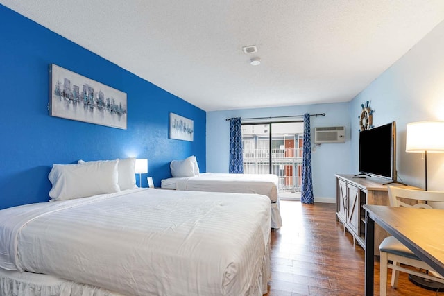 bedroom with a textured ceiling, wood-type flooring, and a wall mounted air conditioner