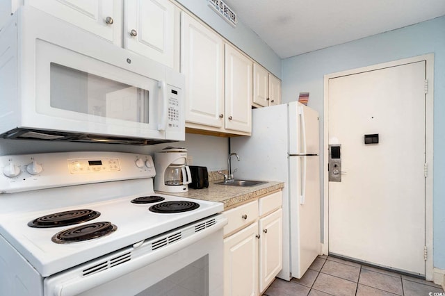 kitchen with white cabinetry, sink, light tile patterned floors, and white appliances