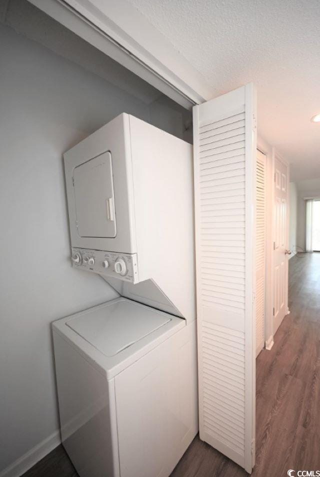 washroom with a textured ceiling, stacked washer / dryer, and dark hardwood / wood-style flooring