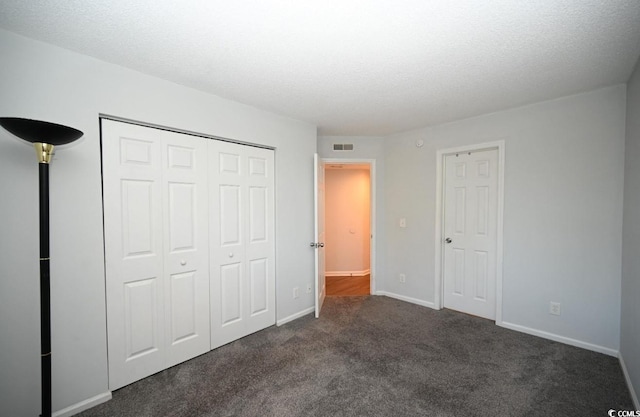 unfurnished bedroom with a textured ceiling, a closet, and dark colored carpet