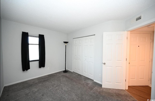 unfurnished bedroom with dark carpet, a textured ceiling, and a closet