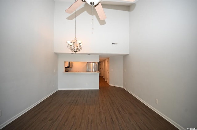 unfurnished living room with ceiling fan with notable chandelier, a towering ceiling, and dark hardwood / wood-style flooring