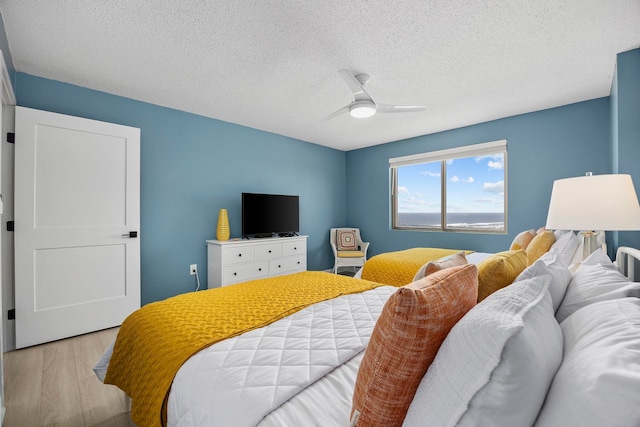 bedroom featuring light hardwood / wood-style floors, ceiling fan, and a textured ceiling