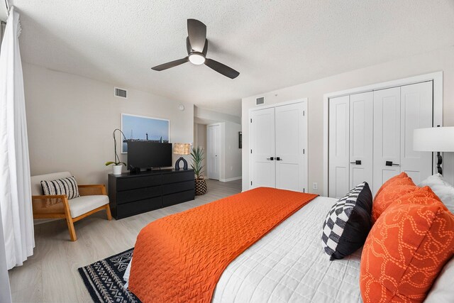 bedroom with ceiling fan, light hardwood / wood-style floors, a textured ceiling, and multiple closets