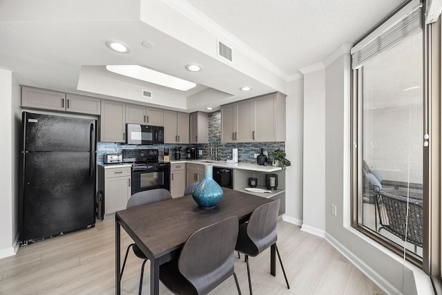 kitchen with backsplash, light hardwood / wood-style flooring, black appliances, a tray ceiling, and gray cabinets