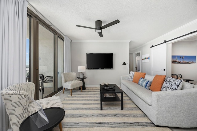 living room with ceiling fan, a textured ceiling, crown molding, and a barn door