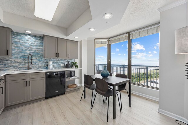 kitchen with decorative backsplash, light wood-type flooring, sink, black dishwasher, and a water view