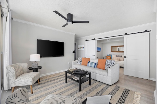 living room featuring light hardwood / wood-style flooring, ceiling fan, ornamental molding, and a barn door