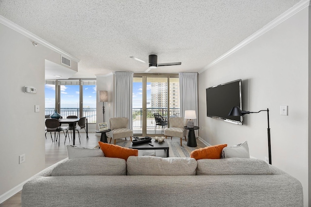 living room featuring expansive windows, light hardwood / wood-style floors, ornamental molding, a textured ceiling, and ceiling fan