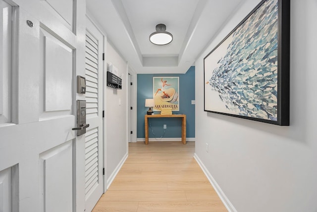 corridor with a raised ceiling and light hardwood / wood-style floors