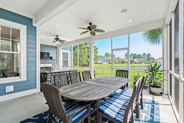 sunroom / solarium with ceiling fan, a stone fireplace, and beamed ceiling