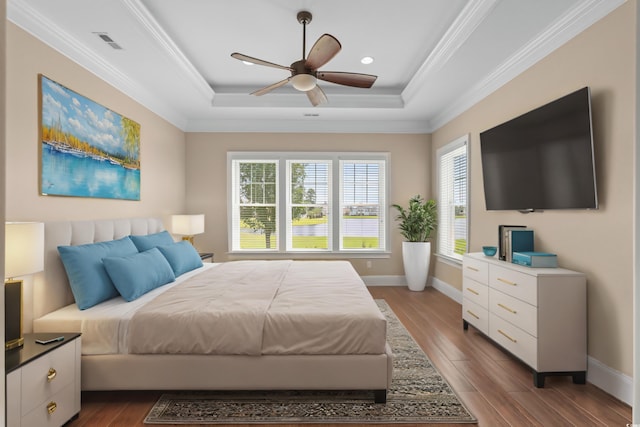 bedroom with ceiling fan, a tray ceiling, wood-type flooring, and multiple windows