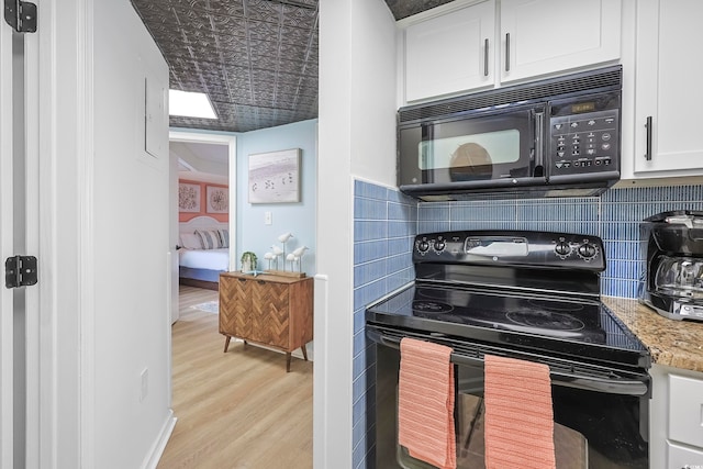 kitchen featuring light stone counters, white cabinets, black appliances, light wood-type flooring, and decorative backsplash