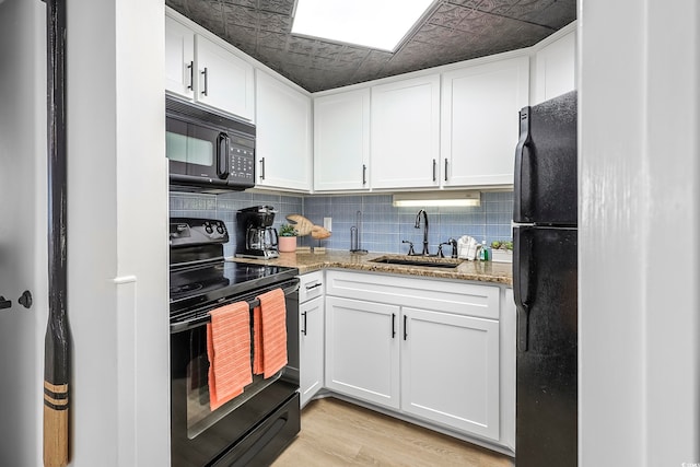 kitchen featuring black appliances, light stone counters, white cabinetry, and sink