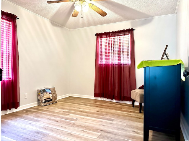 interior space with a textured ceiling, ceiling fan, ornamental molding, and wood-type flooring